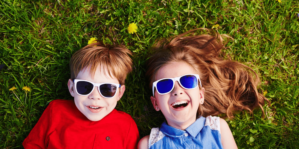 two kids with sunglasses on laughing on the grass
