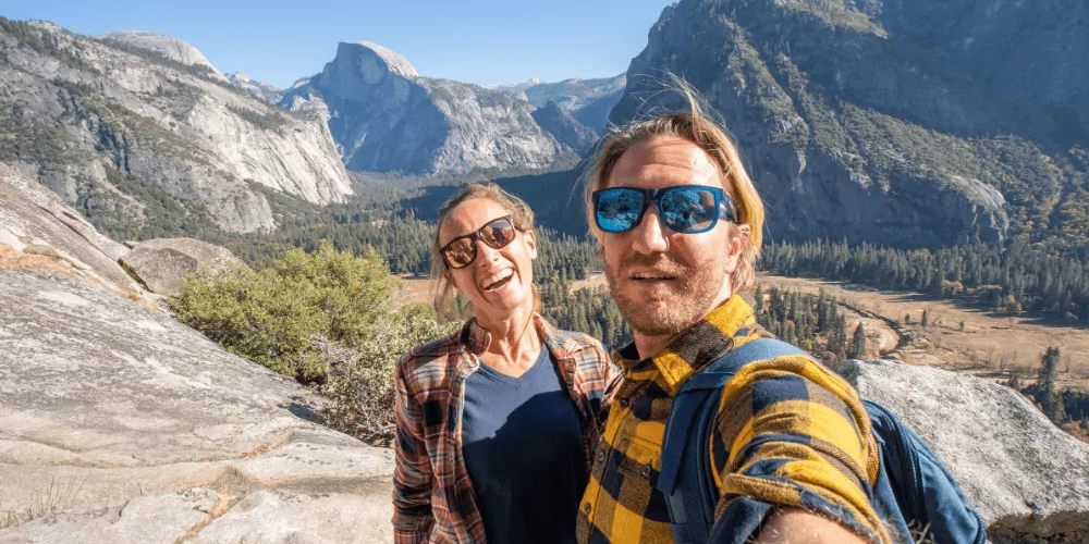 a couple in sunglasses taking selfie in front of half dome view in yosemite