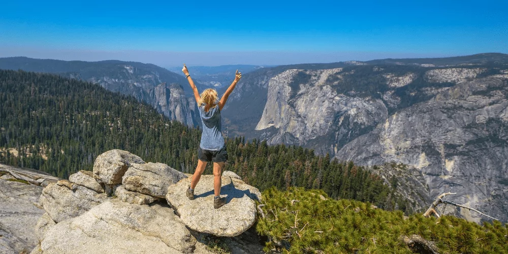 a woman standing on top of a mountain with her arms in the air