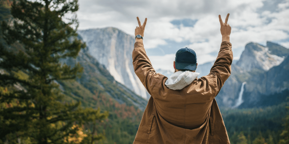 a man with his hands up in the air showing peace sign in front of yosemite valley view