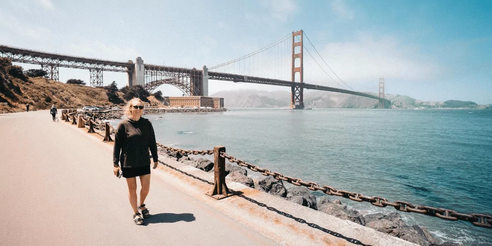 Woman in black hoodie walking near the sf bay with the Golden Gate Bridge on the background