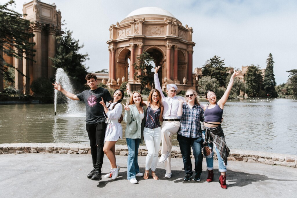 Group of friends standing in front of Palace of fine arts with their hands raised up in the air