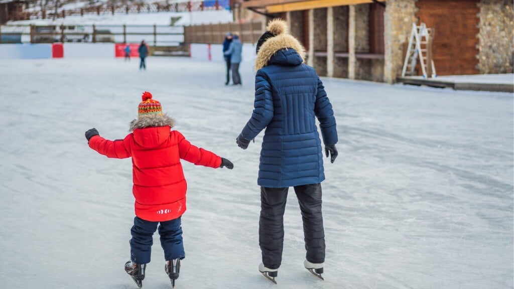 a woman in a blue coat skating beside a kid in scarlet red jacket