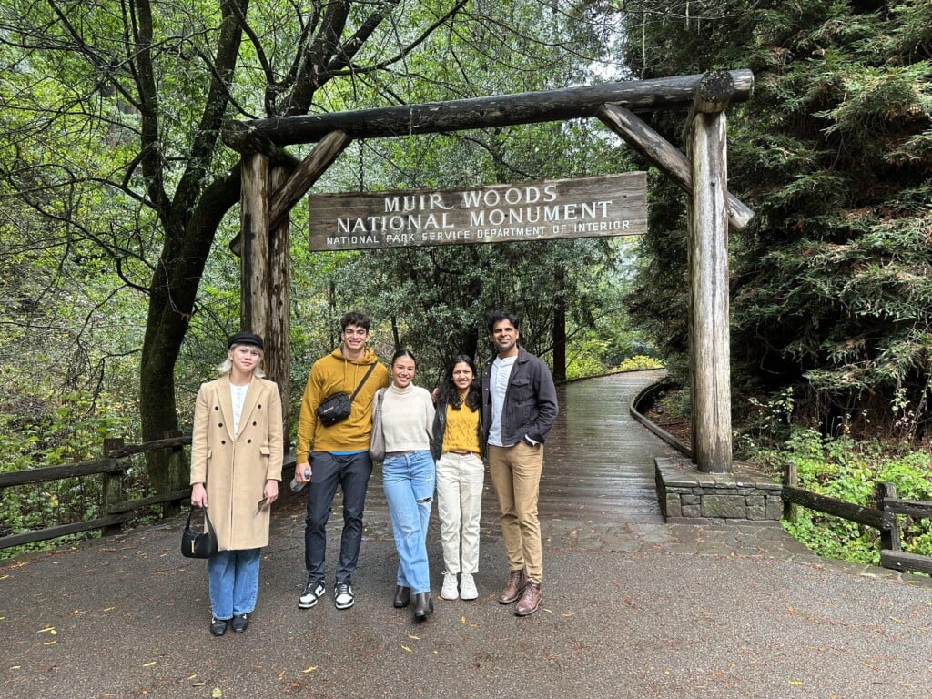 group of people taking a photo in front of the muir woods signage