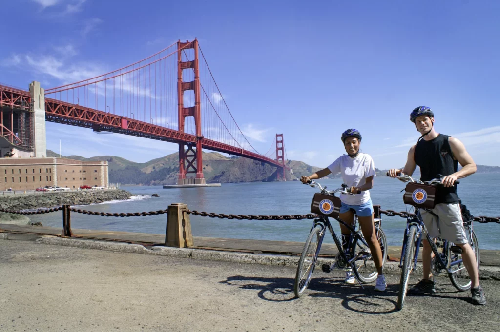 a boy and a girl standing with their bikes in front of the Golden Gate Bridge