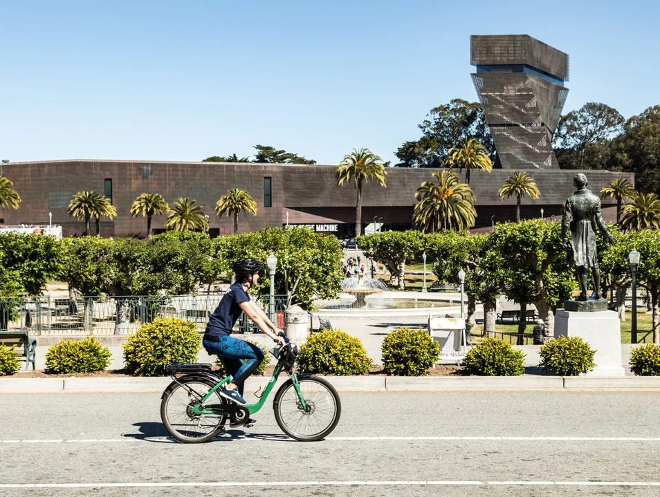 a person with helmet on riding a bike in front of de Young museum in the Golden Gate Park