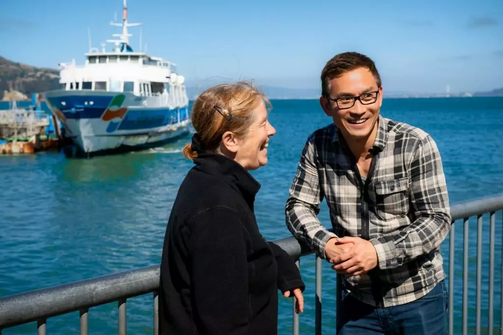 a man and a woman standing next to each and laughing near a body of water