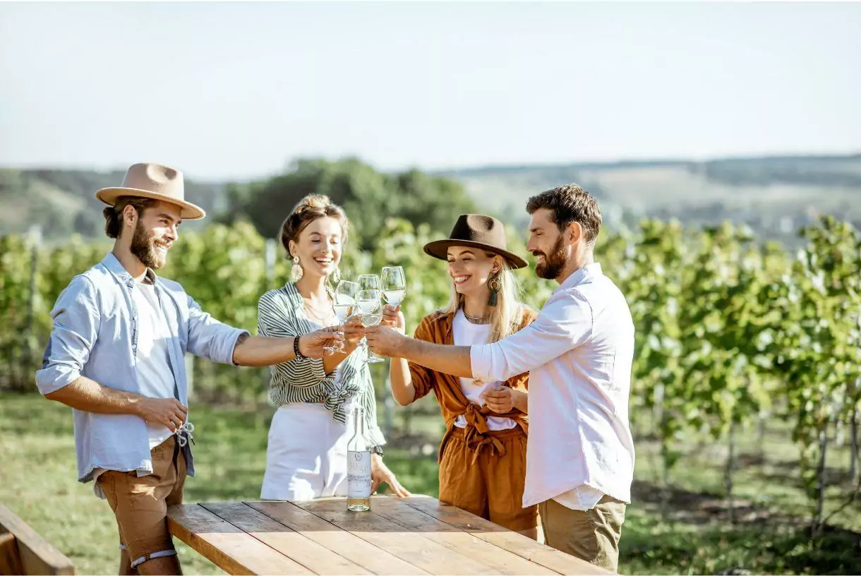 people standing around a wooden table and toasting in the vineyard