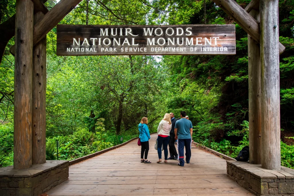 group of people standing next to the muir woods entrance sign