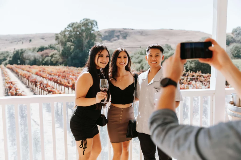 three friends posing on the winery's porch in front of vineyards