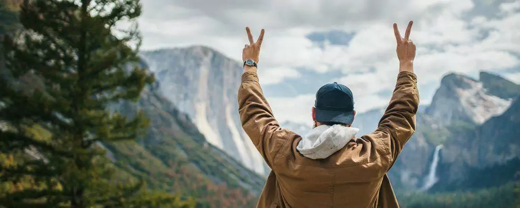 a man with his hands up in the air showing peace sign in front of yosemite valley view