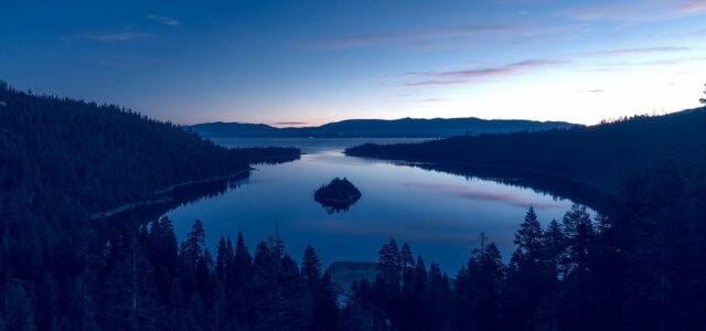 emerald bay framed by trees at sunset.