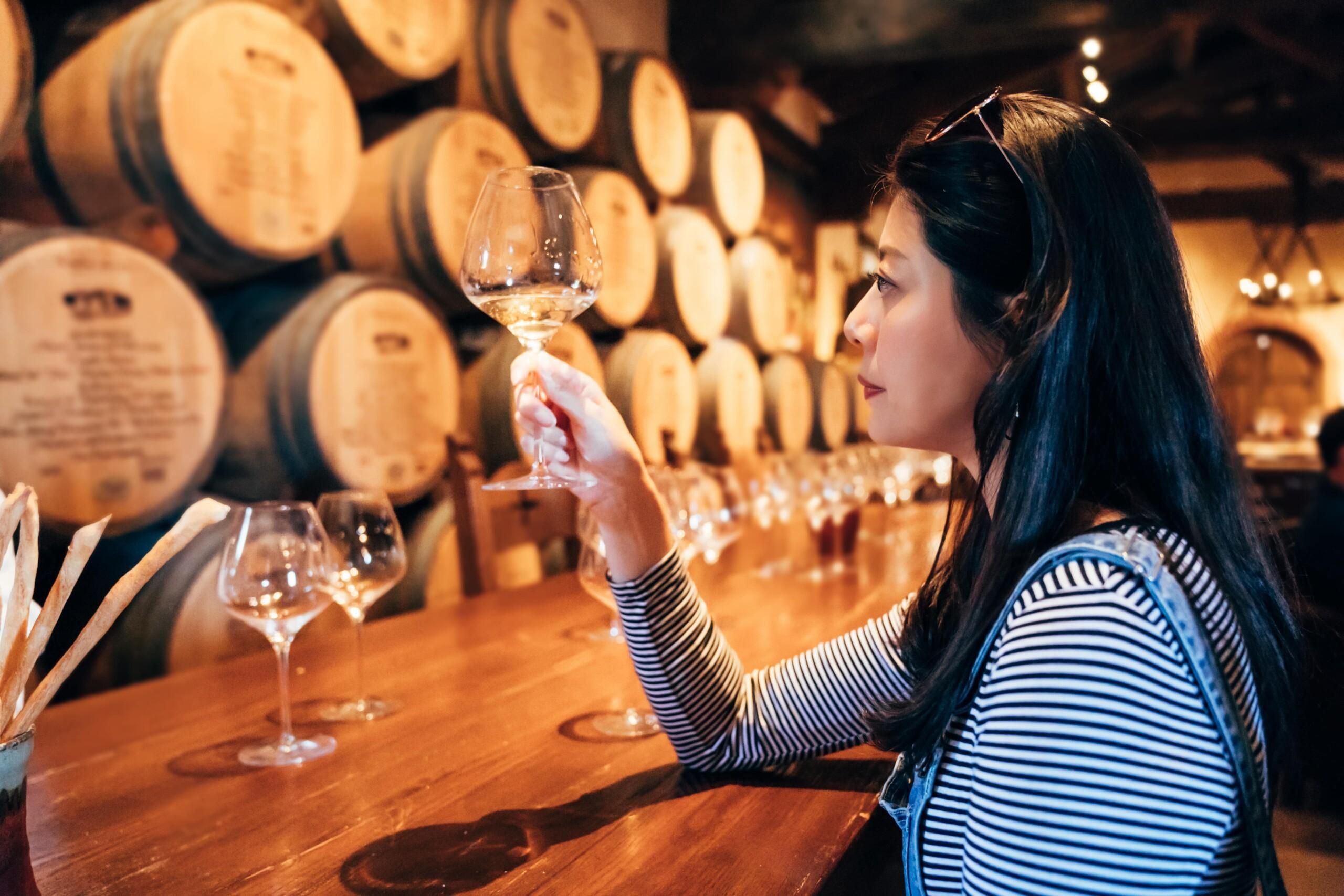 brunette woman in a striped shirt tastes white wine at a winery bar