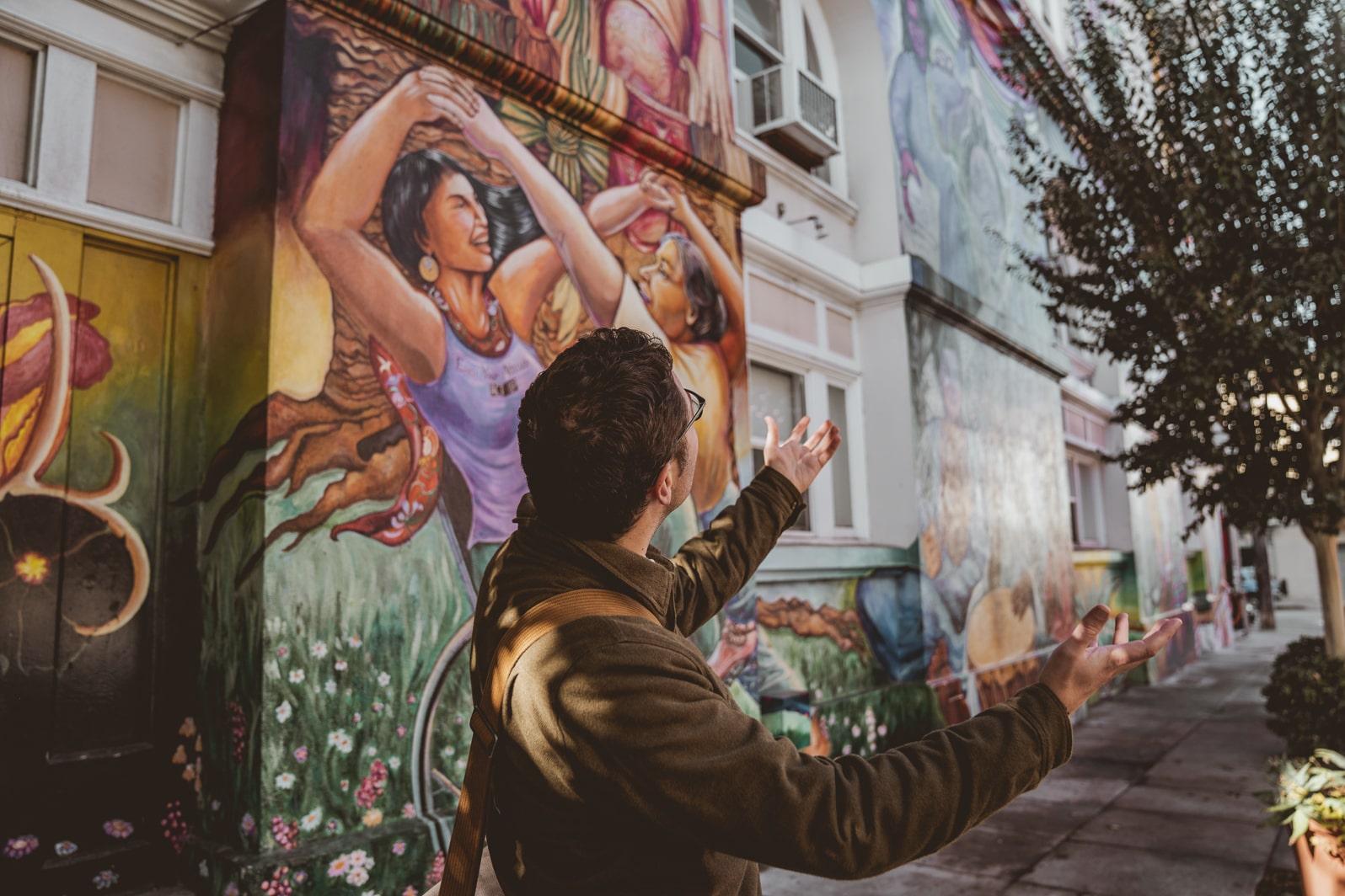 man showing mural of dancing women in mission district