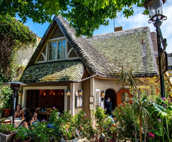 A quaint bungalow-like restaurant in the city of Carmel-by-the-Sea, surrounded by multiple plants.