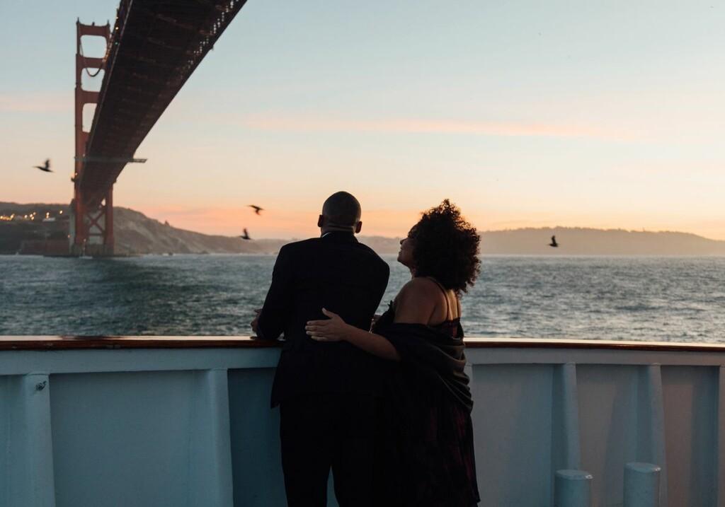 a couple watching the sunset under the golden gate bridge