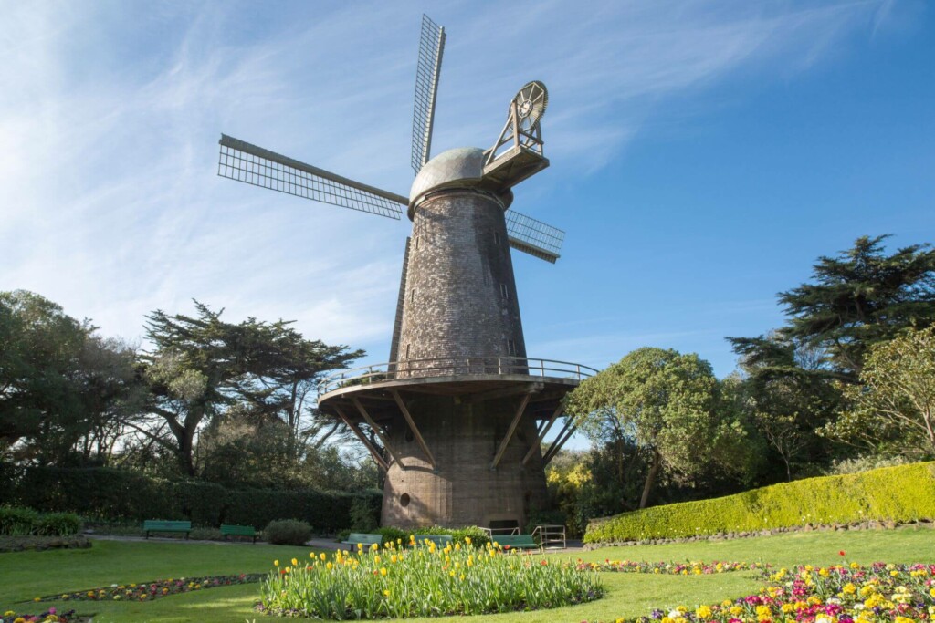 a tall windmill surrounded by green grass and flowers 