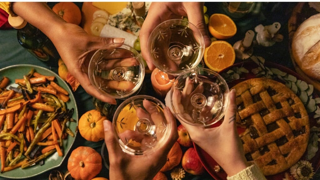 people raising glasses of white wine in a celebratory atmosphere around a dinner table