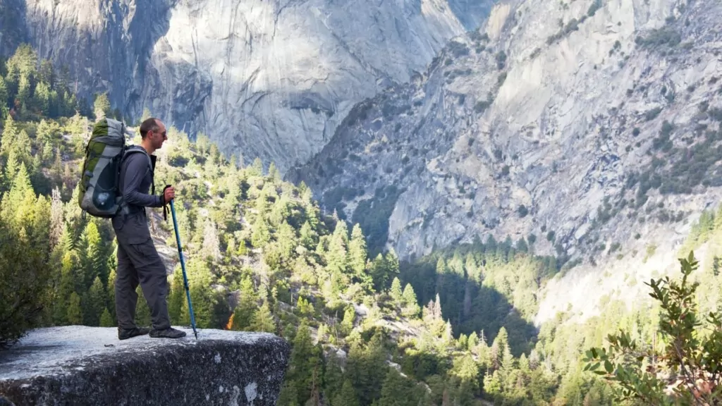 a man with hiking poles on the edge of a cliff overlooking yosemite valley