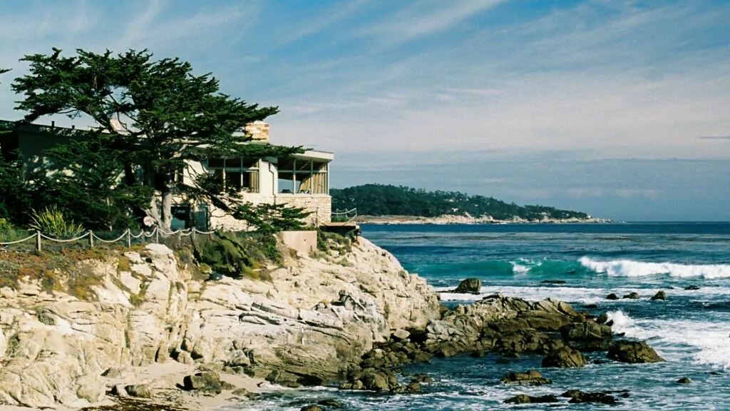 A lone cypress and a house on a rocky cliff overlooking the ocean