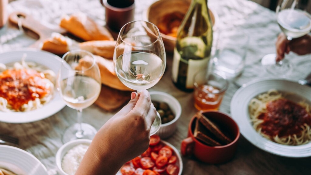 a glass of white wine with fine dining foods on the background