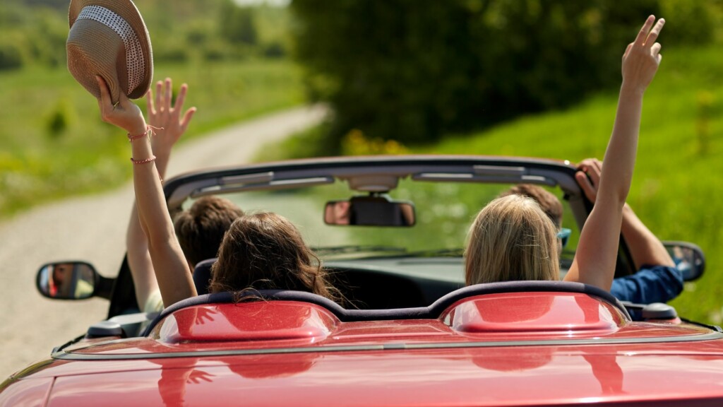 two girls at the backseat of a red car with their hands raised who are driving to san francisco from muir woods