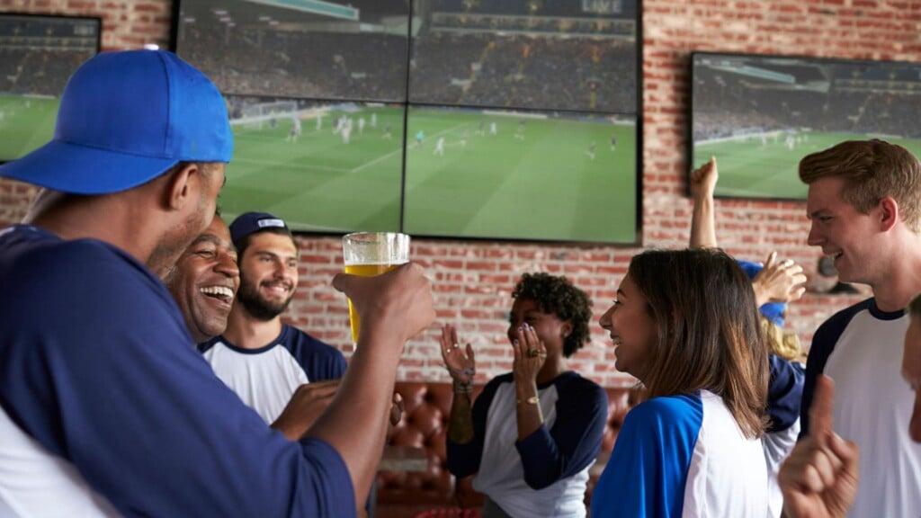 a group of people smiling while watching sports on a television screen during fall season in San Francisco