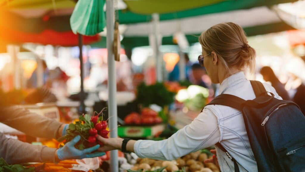 a woman in a white shirt picking up beetroot at a market 