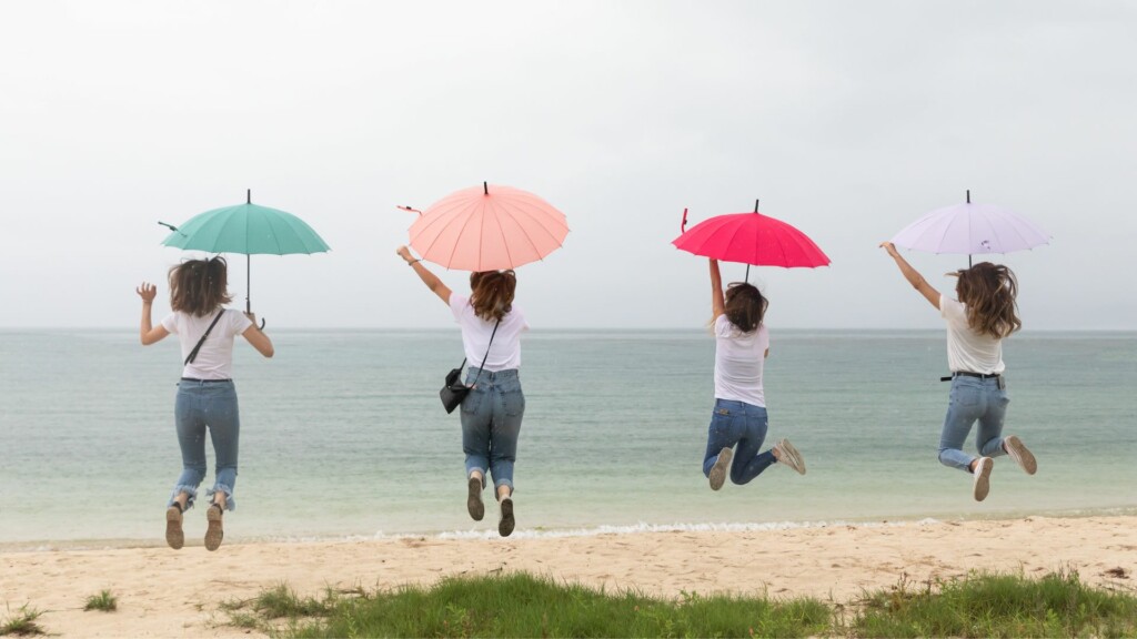 four women holding umbrellas by the beach on a rainy day