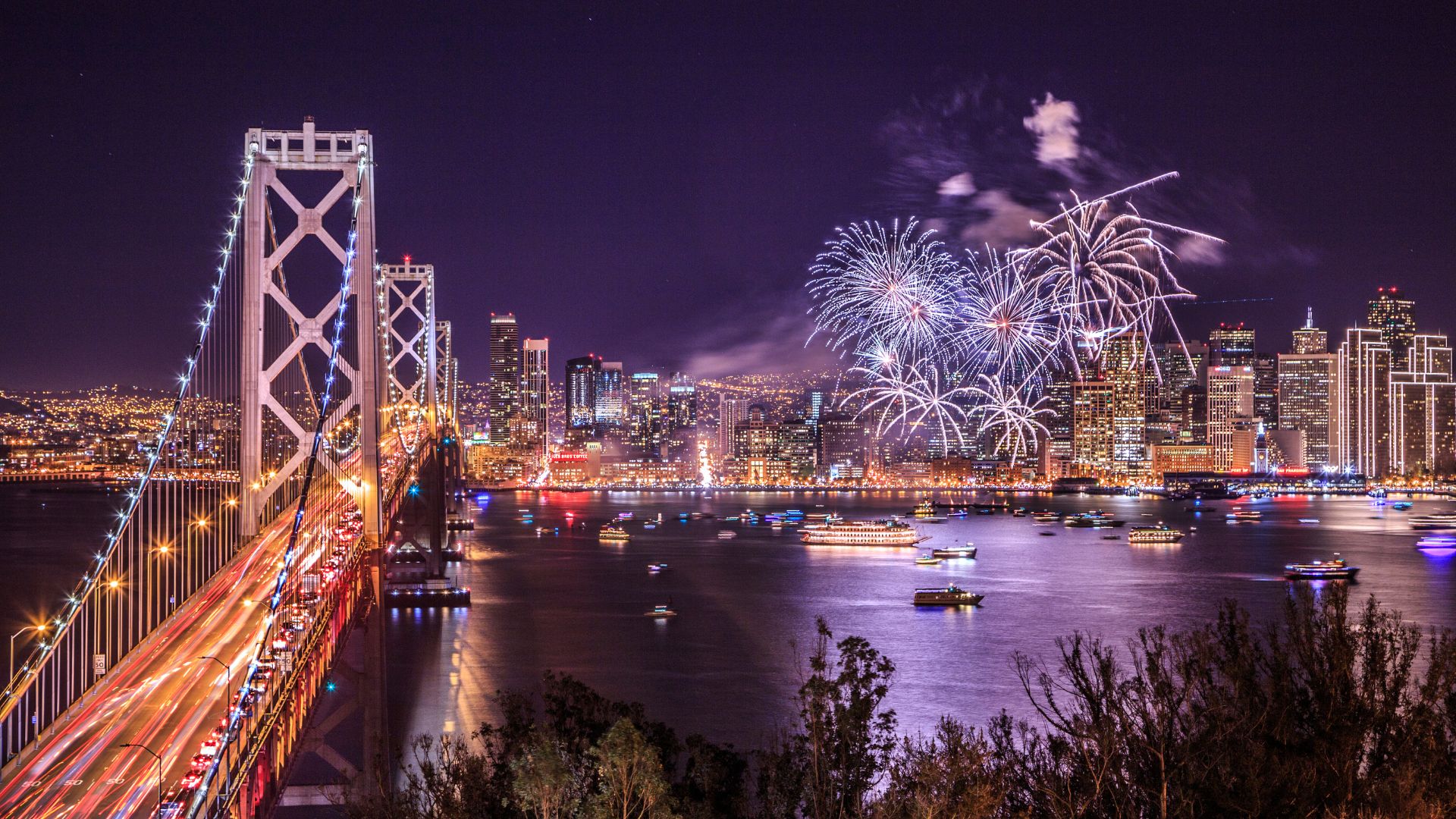 aerial view of San Francisco bridge at night with colorful fireworks in the background