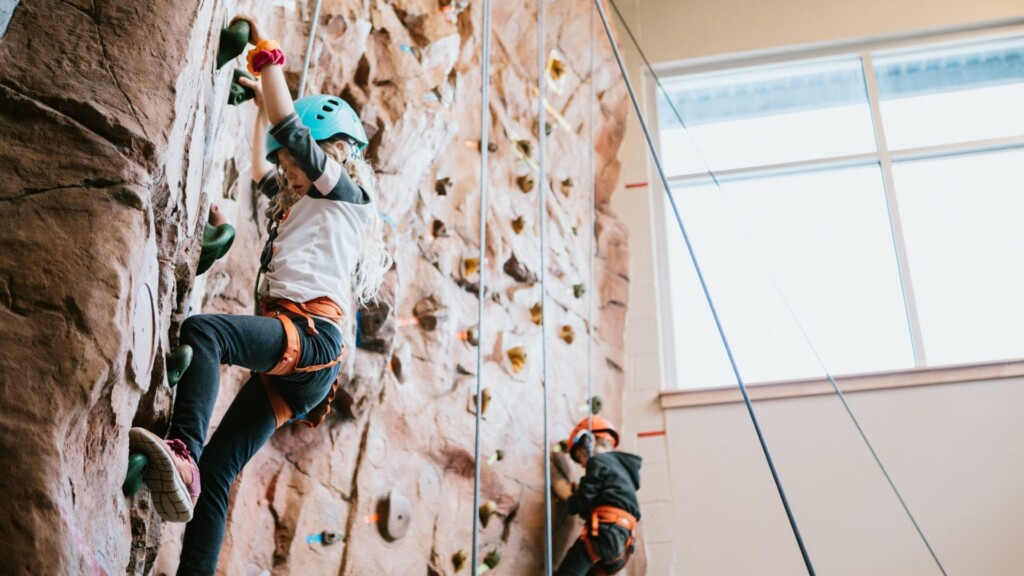 two kids with helmets climbing up a wall of rocks on a rainy day