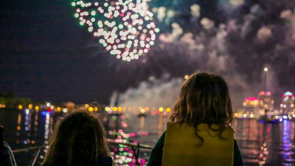 two girls watching colorful fireworks by the bay