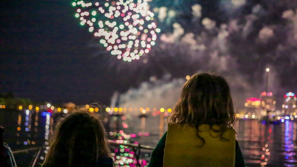 two girls watching colorful fireworks by the bay 