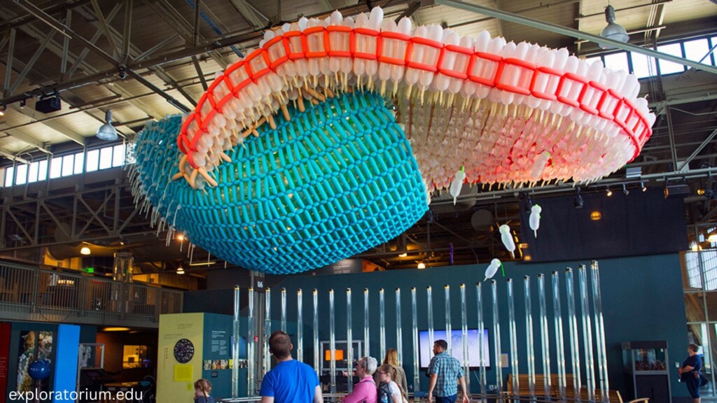 a man in a blue shirt staring up at a plastic balloons made into art on a rainy day