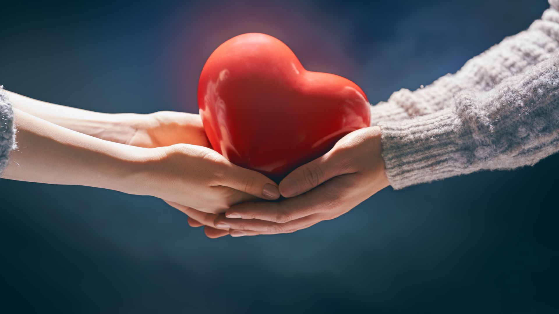 two people holding a red heart shape figurine with their hands