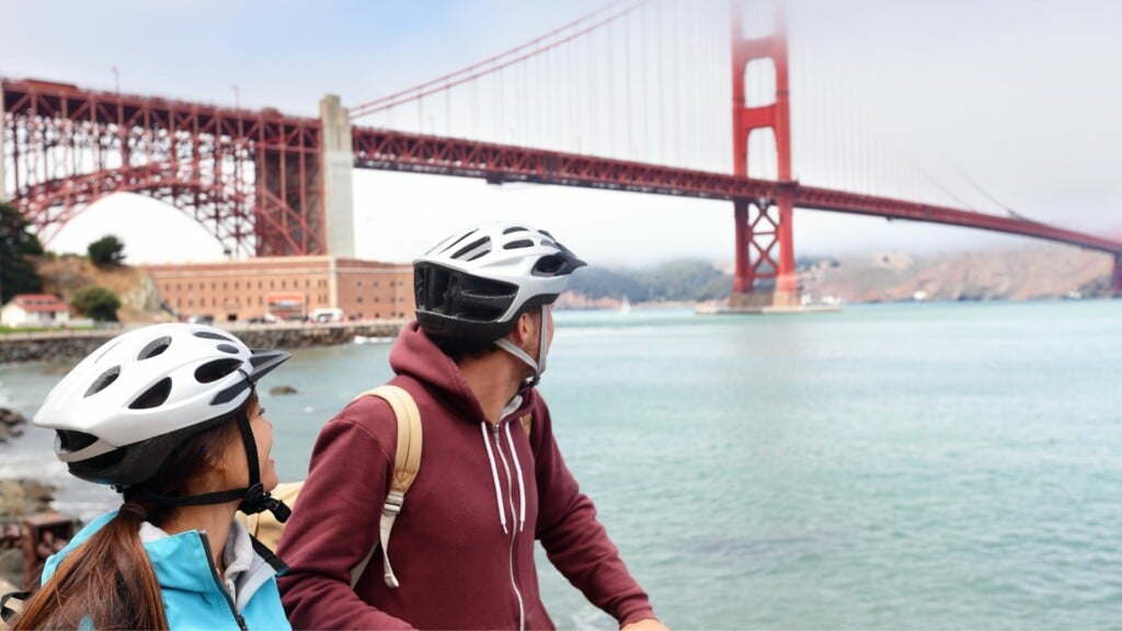 a couple in helmet riding a bike with golden gate bridge as background