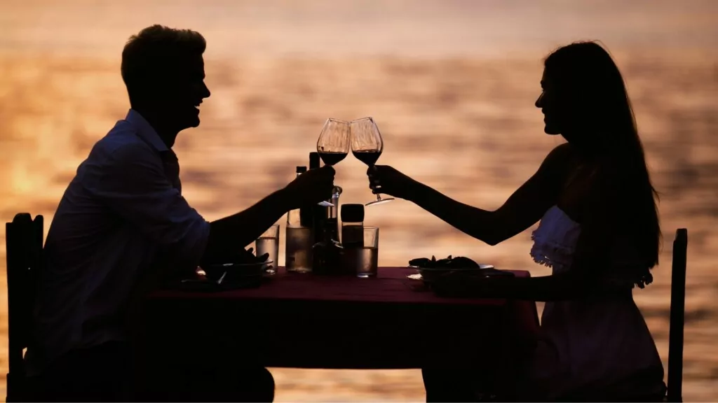 a silhouette of a couple toasting their wine glass 