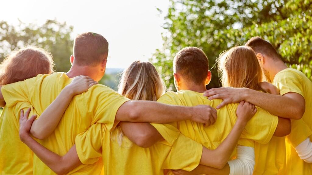 A group of friends in matching yellow shirts is embracing each other outdoors, symbolizing togetherness and unity.
