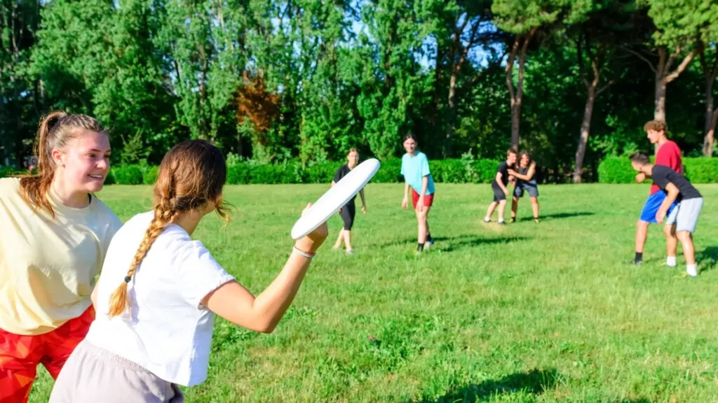 A group of friends enjoys an ultimate frisbee game in a sunny park, surrounded by lush greenery.