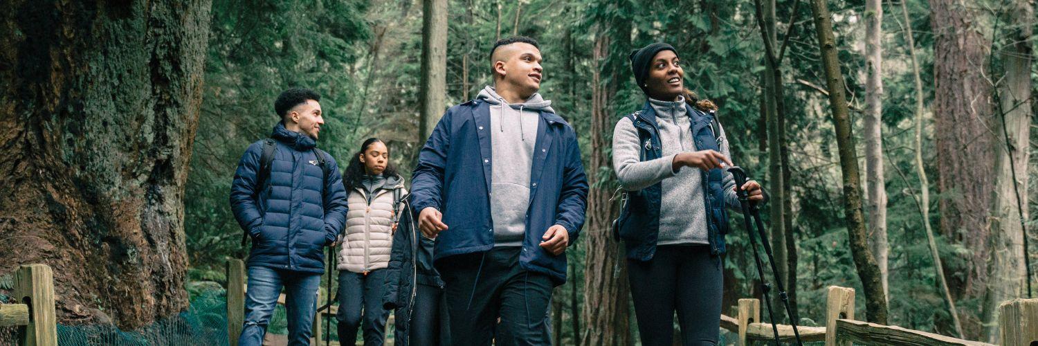 A group of four friends hiking through a dense forest, dressed in warm outdoor clothing, with smiles on their faces