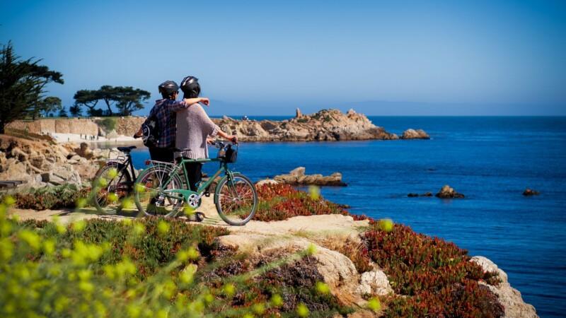 A couple with bikes enjoys an ocean view from a scenic cliffside trail.