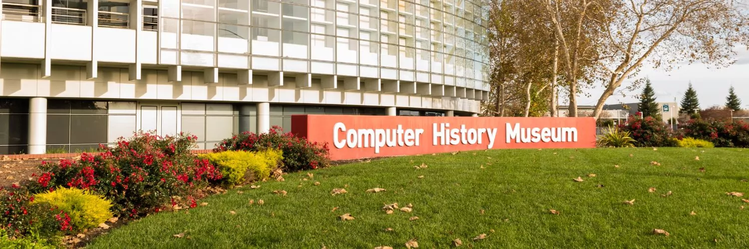Exterior view of the Computer History Museum with a red sign and modern glass-front building surrounded by trees and landscaping