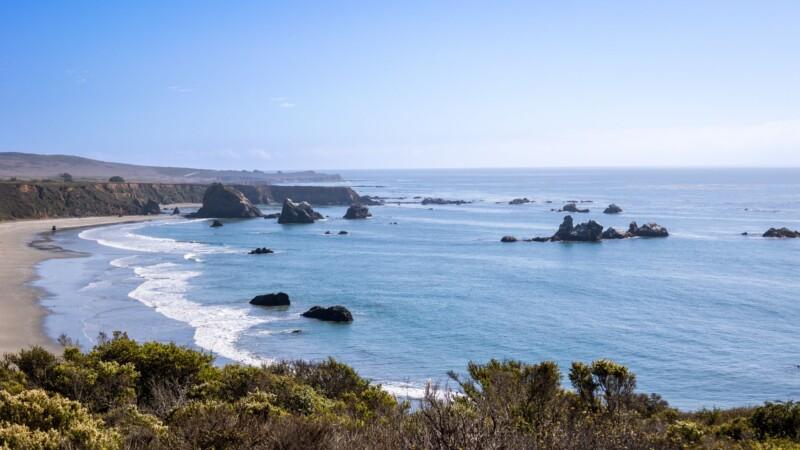 Panoramic view of the California coastline at Sonoma Coast State Park, with rocky outcroppings in the Pacific Ocean and waves gently reaching the sandy shore