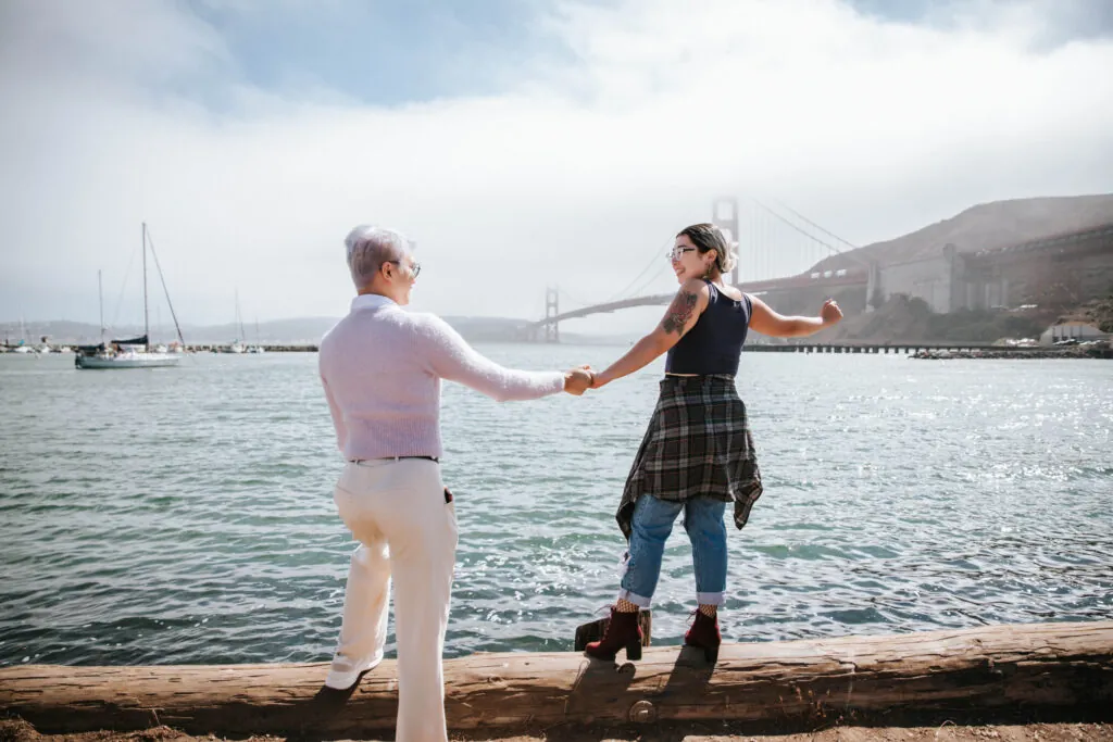 two people holding hands by the water near the Golden Gate Bridge